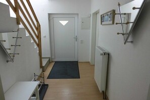A narrow hallway with a wooden staircase on the left, a door with a triangular window at the end, and a radiator on the right. - Holiday home with 3 bedrooms (Dornumersiel)
