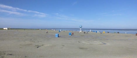A sandy beach with a clear sky, a few scattered blue containers, and a distant spherical structure.
