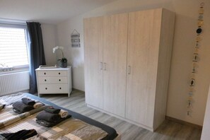 Ein Schlafzimmer mit Bett, Nachttisch, Kleiderschrank und einem Fenster mit Vorhängen.