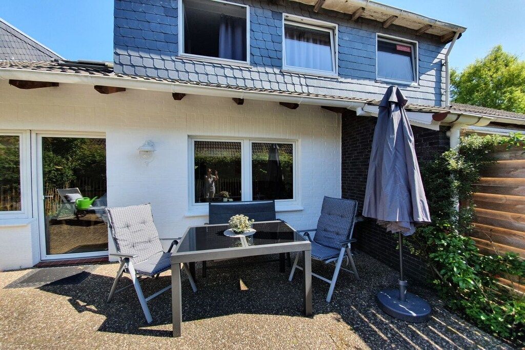Un patio con una mesa y sillas, una sombrilla y vista a una casa con ventana y puerta.
