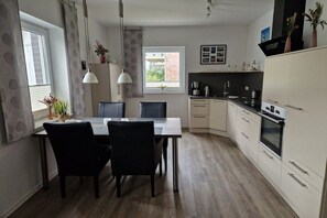 Eine moderne Küche mit Essbereich, ausgestattet mit einem Tisch, Stühlen, einem Fenster mit Vorhängen und einem Einbauofen.