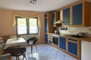 A kitchen with blue cabinets, a white countertop, and a dining area with a table and chairs. - Holiday apartment with 2 bedrooms (Graach)
