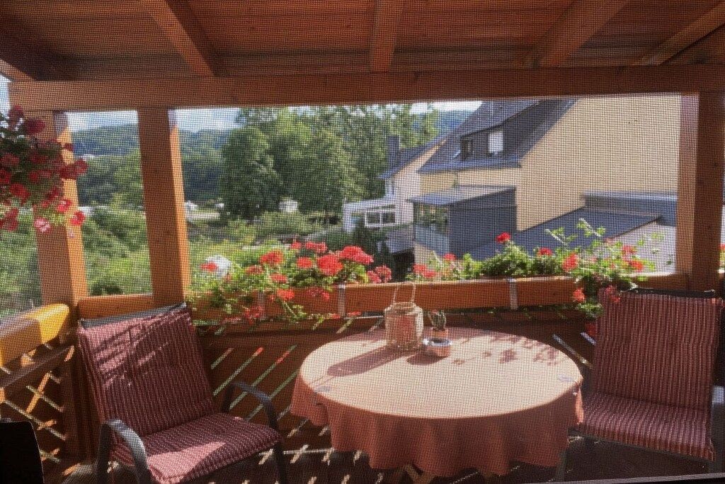 An outdoor patio with a round table and chairs, surrounded by potted plants and flowers.