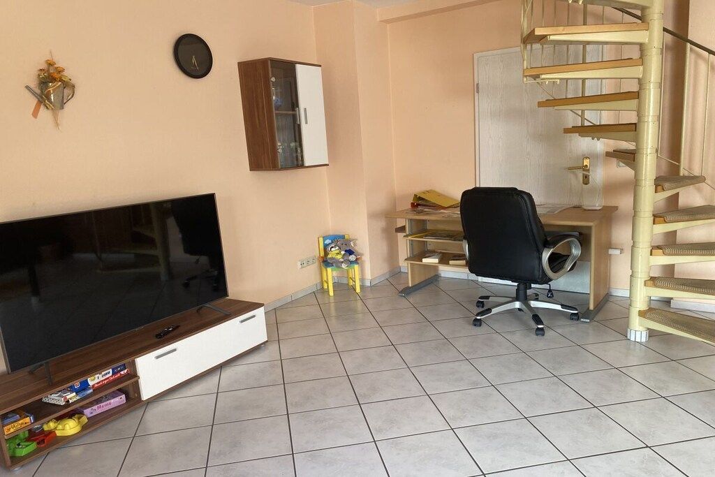 Een kamer met een flatscreen televisie, een houten kast, een bureau met stoel en een wenteltrap.