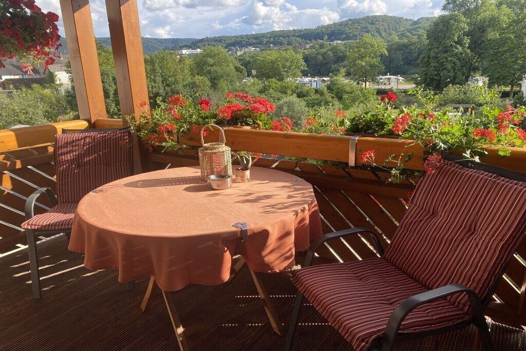 Un espace extérieur aménagé avec une table ronde, des chaises à rayures et une vue sur la verdure et les collines.