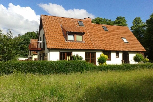A two-story house with a sloped roof, a small balcony, and a well-maintained garden. - Holiday apartment with 1 bedroom (Bremen)