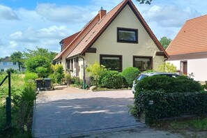 Una casa residencial con techo inclinado, un camino de entrada pavimentado y un coche estacionado allí.