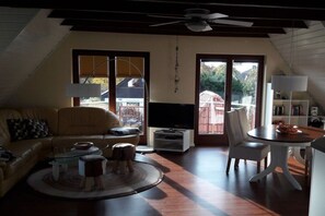 Ein Wohnzimmer mit Sofa, Couchtisch, TV-Schrank und einem Essbereich mit Tisch und Stühlen.