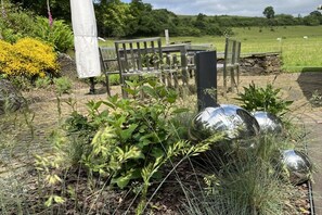 Een tuin met een bankje, een metalen sculptuur en een pad.