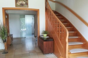 Eine Treppe mit hölzernen Geländern führt zu einer oberen Etage, ein Flur mit einer Tür und eine Topfpflanze auf einem Schrank.