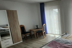 Ein Schlafzimmer mit einem Bett, einem Kleiderschrank, einem Schreibtisch mit Stuhl und einem Fenster mit Vorhängen.