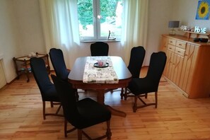 A dining area with a wooden table and six chairs, a window with curtains, and a cabinet with a sunflower decoration. - Holiday home with 4 bedrooms (Ladbergen)