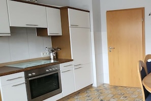 Eine kleine Küche mit weißen Schränken, einer Holz Arbeitsplatte, einem eingebauten Ofen und einer gefliesten Spritzschutzwand.