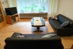 A living room with a sofa, a coffee table, a television, and a window with a view of a garden. - Holiday home with 4 bedrooms (Ladbergen)