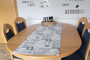 Ein Esstisch mit einer gemusterten Tischdecke, Holzstühle und eine Wand mit Schildern für Kaffee und Schokolade.