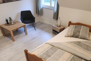A bedroom with a bed, a bedside table, a chair, a window, and a small table with a plant. - Holiday home with 4 bedrooms (Ladbergen)