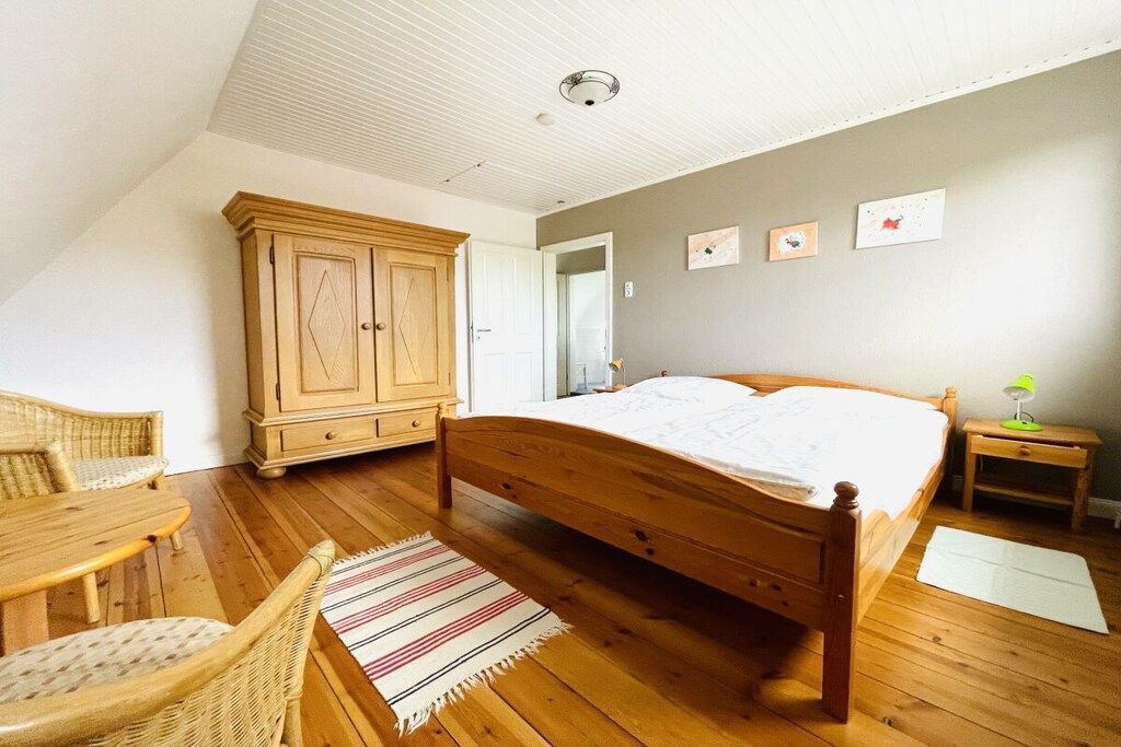 Een slaapkamer met een houten bed, een kledingkast, een stoel en een klein tafeltje.