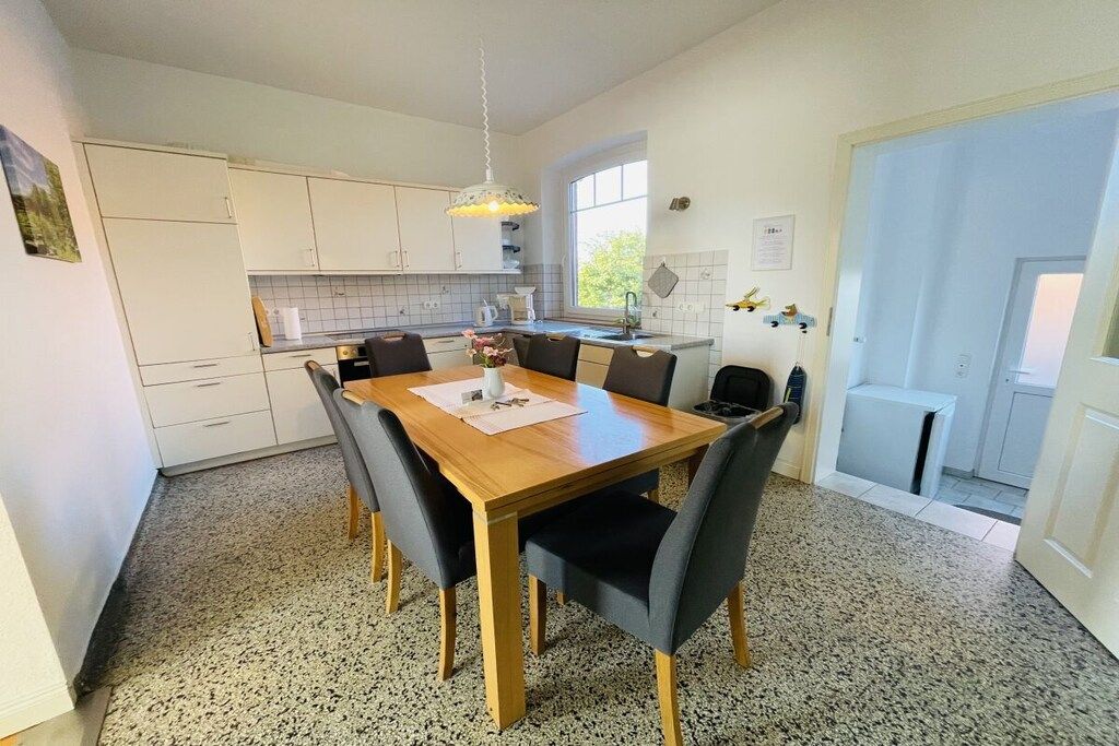 A compact kitchen with a dining table and chairs, a hanging light fixture, and a window providing natural light.