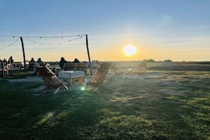 An outdoor seating area with tables and chairs, a string of lights, and a view of the sunset. - Holiday home in Fehmarn with swimming pool (Fehmarn)