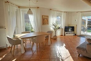 Ein Essbereich mit Tisch, Stühlen, einem Fernseher und einer Zimmerpflanze.