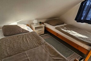 Une petite chambre agréable, dotée de deux lits, d’une table de chevet avec une lampe et d’une fenêtre avec des rideaux.