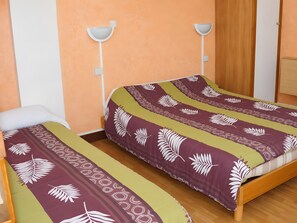 A room with two single beds, each with a patterned bedspread, a wooden wardrobe, and a white wall-mounted light fixture. - Holiday Home 'Chambre Pour 3 Au RDChaussée' with Mountain View, Shared Terrace and Wi-Fi (Font-Romeu-Odeillo-Via)