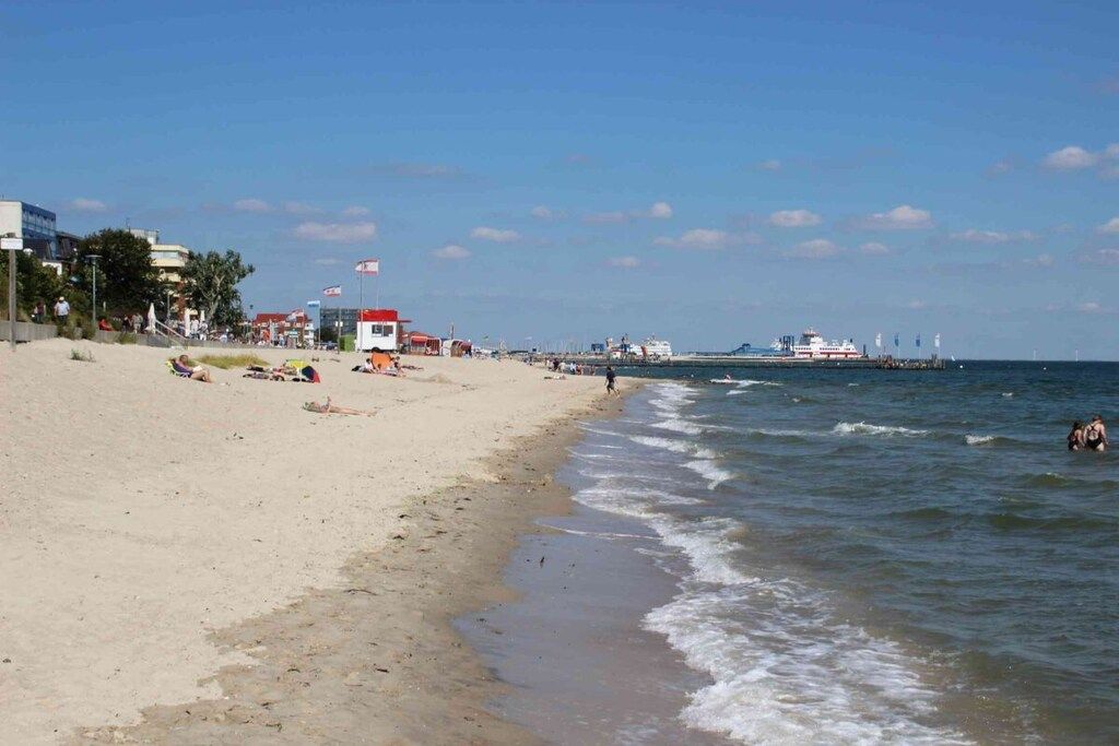 A beach with a lifeguard tower, a pier, and a large ship in the distance.