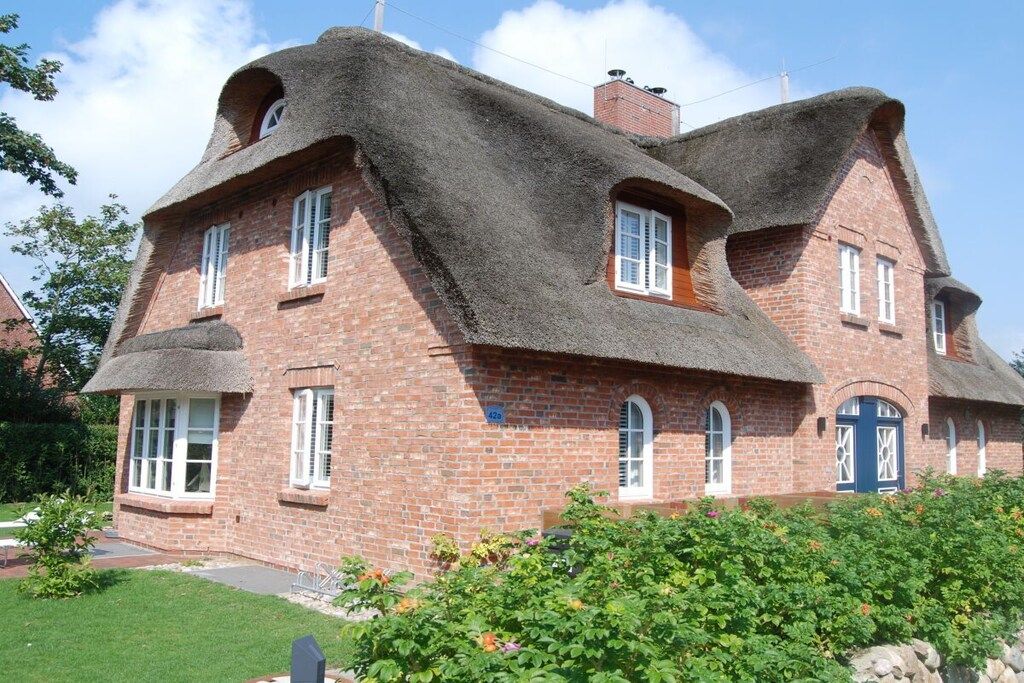 Een huis van baksteen met rieten dak en meerdere ramen.