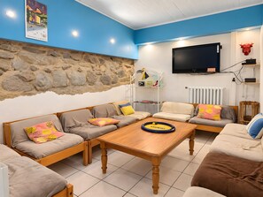 A living room with a stone wall, a television, and a wooden coffee table. - Holiday Home 'Chambre Pour 4 Au RDChaussée' with Mountain View, Shared Terrace and Wi-Fi (Font-Romeu-Odeillo-Via)