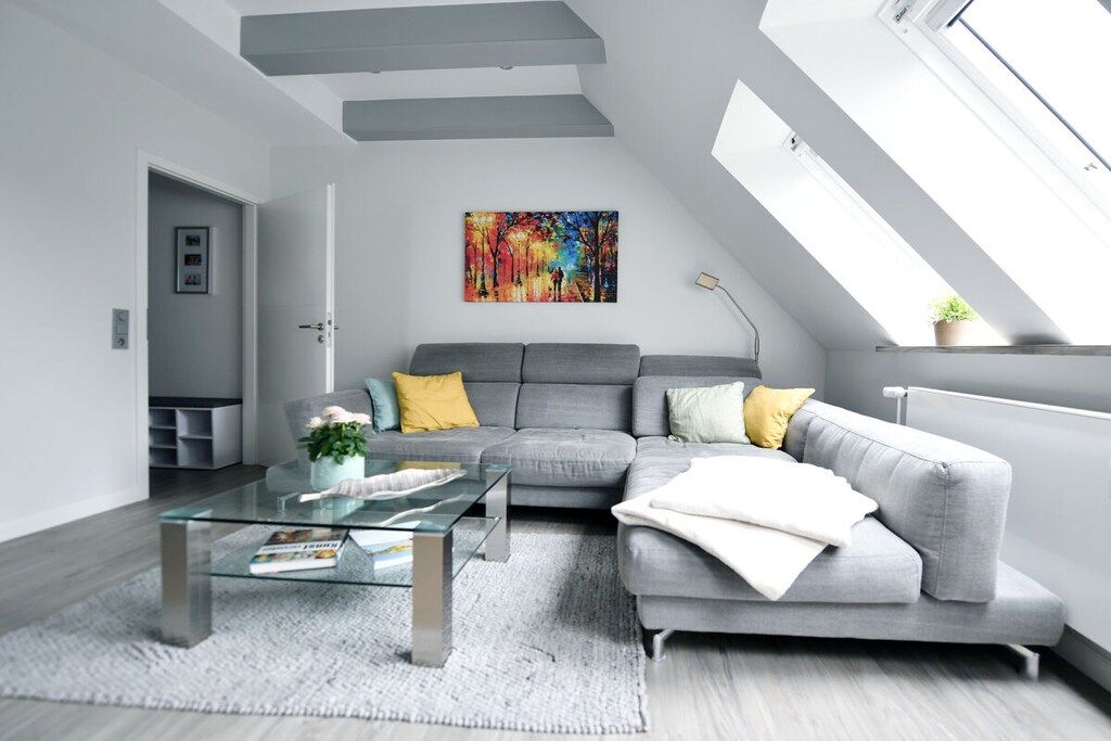 Un salon moderne avec un canapé gris, une table basse en verre et un tableau coloré accroché au mur.