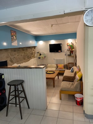 Un espace de vie compact comprenant un coin cuisine, un ensemble de canapés, une table à manger et un téléviseur fixé au mur.