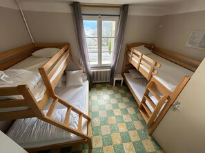 Een kamer met twee stapelbedden, een radiator, een raam met gordijnen en een geruit vloertje.