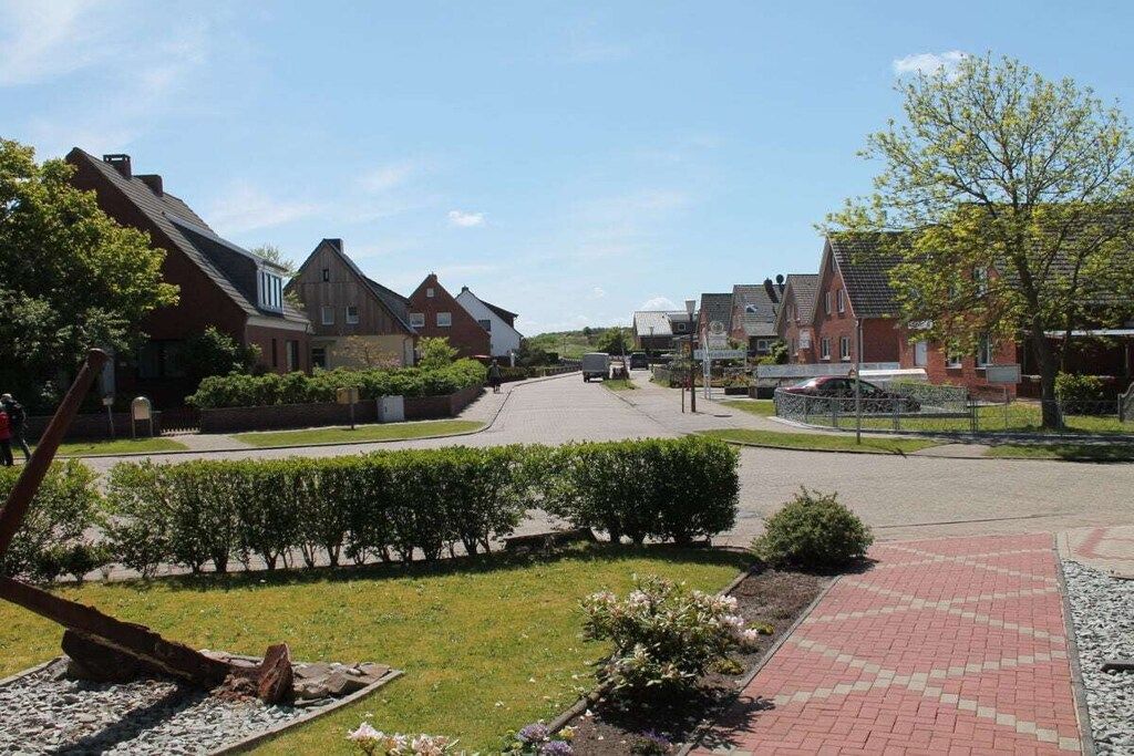 Una calle residencial con casas, una vía pavimentada y un área ajardinada con arbustos y flores.