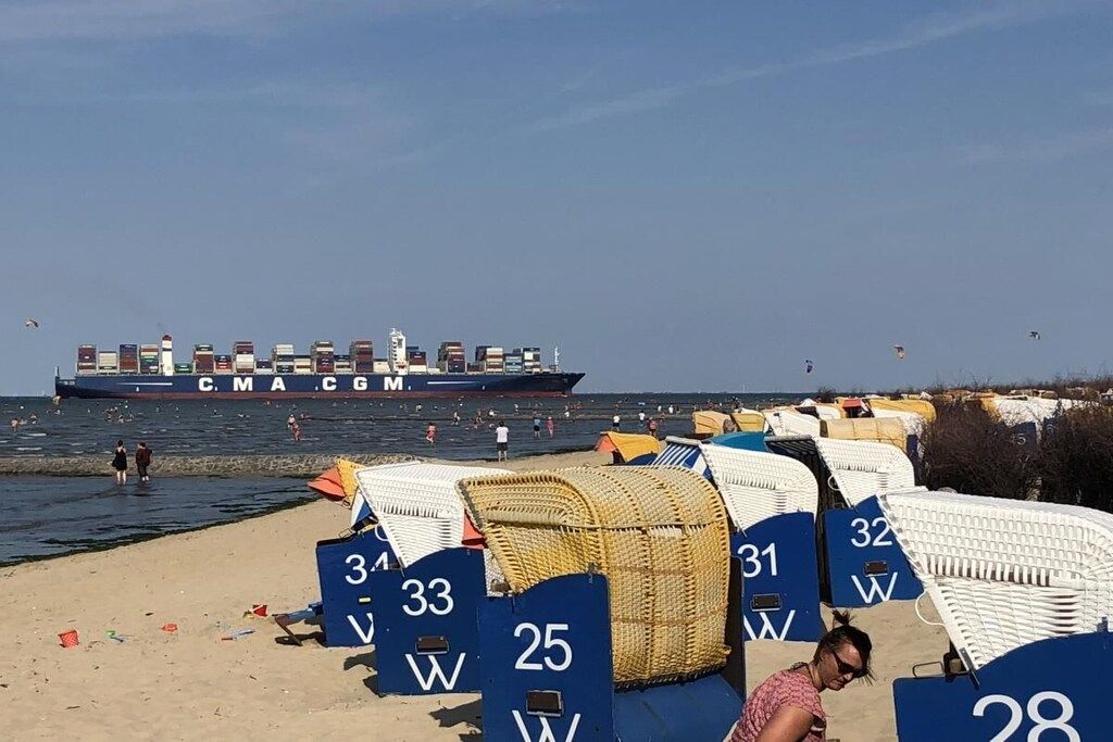 A beach with rows of numbered beach chairs and a large cargo ship in the background.