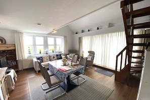 A spacious living room with a dining area, a staircase, and a view of the outdoors. - Swallow's Nest Pavilion (Cuxhaven)