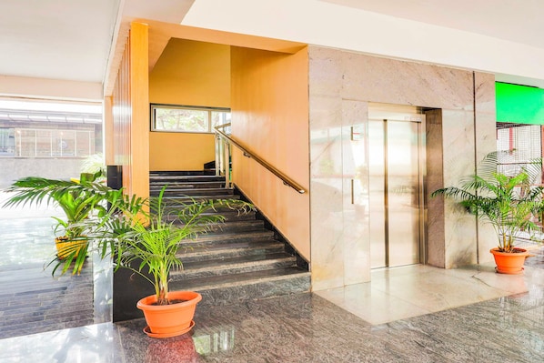 A modern indoor staircase with a handrail, a glass elevator, and potted plants.