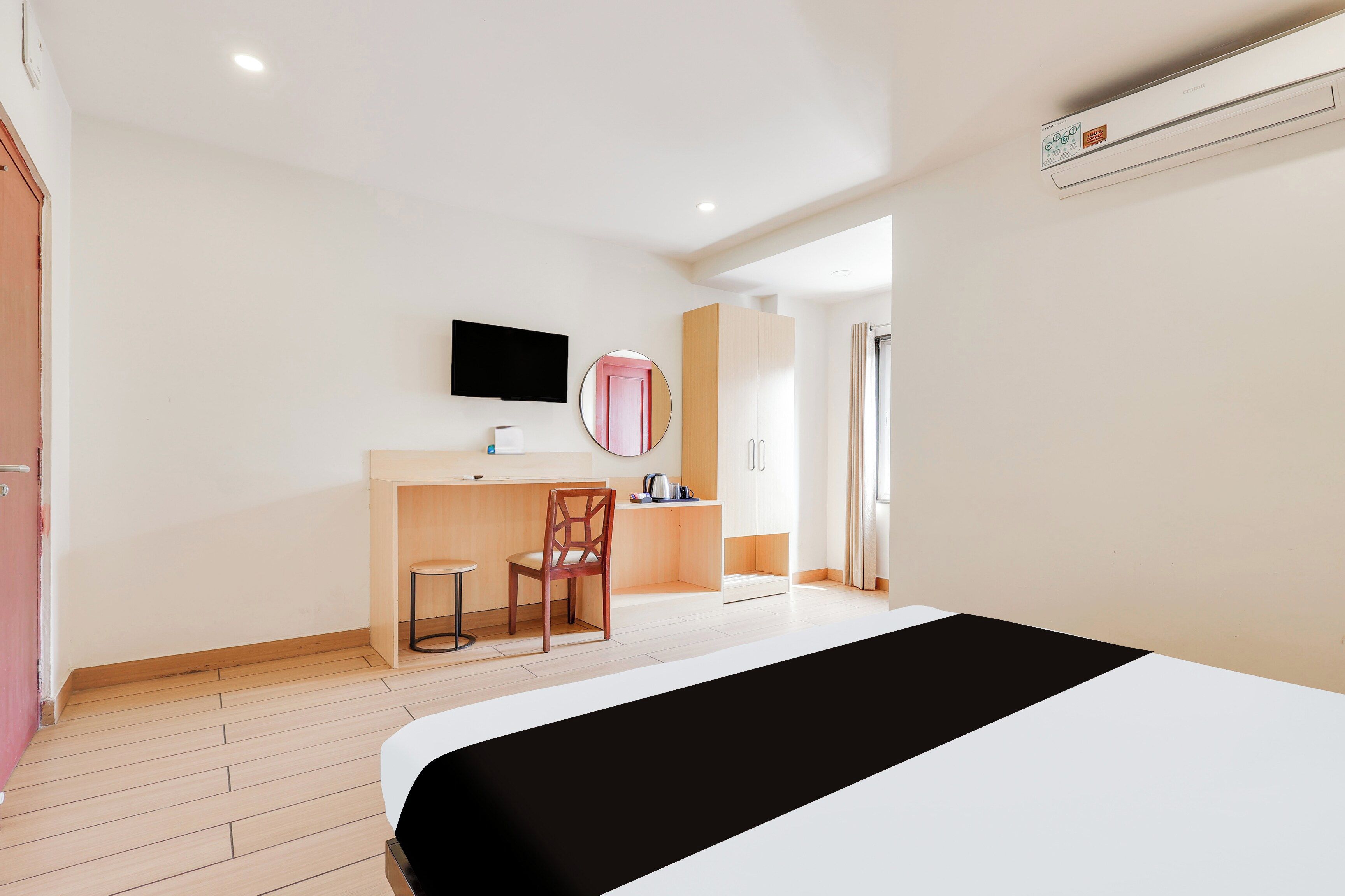 A hotel room with a bed, a desk, a chair, a television, and a mirror.