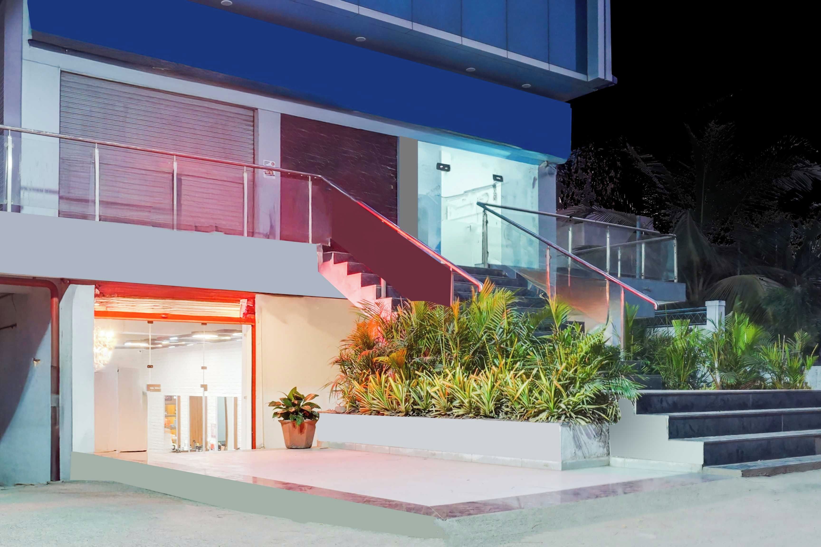 A modern two-story building with a glass facade, a red staircase, and a well-maintained garden area.