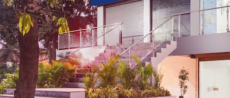 Un edificio moderno con una escalera que conduce a un nivel superior, rodeado de vegetación y un árbol.