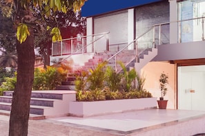 Un edificio moderno con una escalera que conduce a un nivel superior, rodeado de vegetación y un árbol.