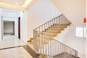 Eine Treppe mit Metallgeländer führt zu einer oberen Etage, links eine Tür und rechts ein Fenster.