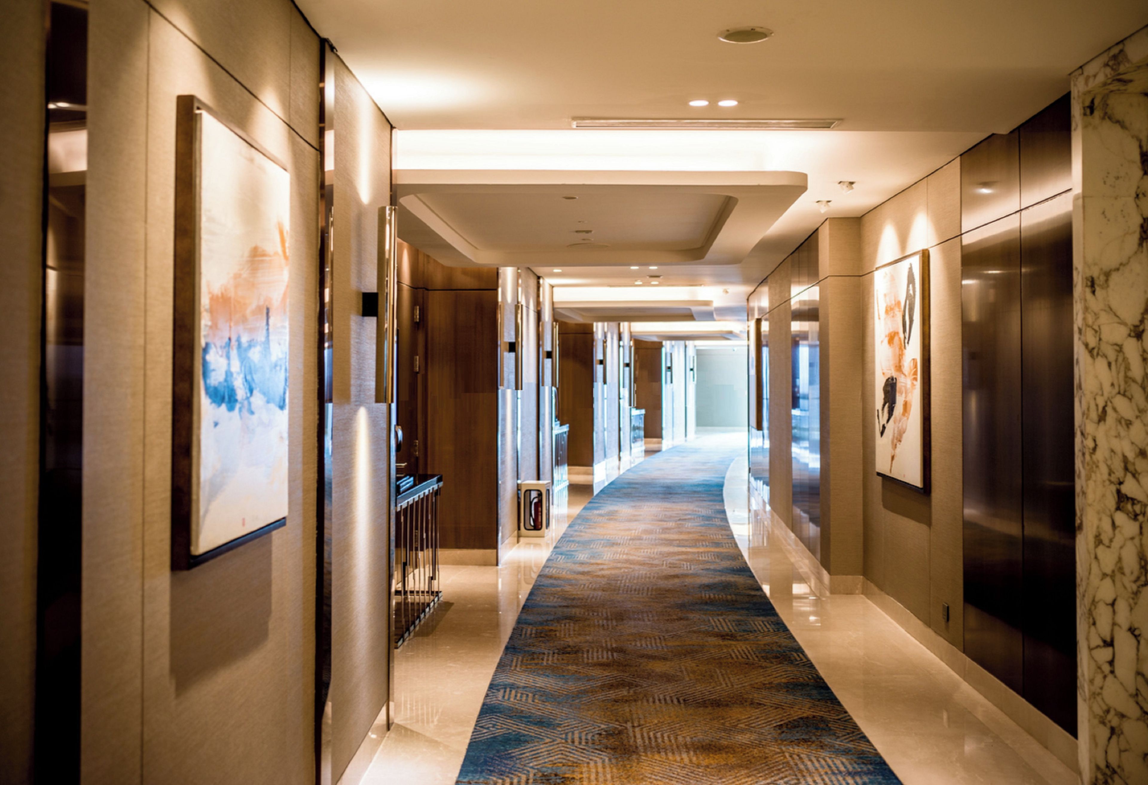 Een hotelgang met een kamerbreed tapijt, kunstwerken in lijsten aan de muur en een schoon, modern design.