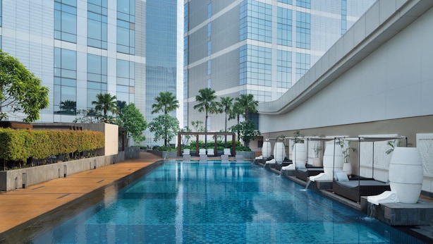 A modern indoor pool with a tiled floor, surrounded by lounge chairs and palm trees. - Intercontinental Residence Jakarta Pondok Indah (Jakarta)