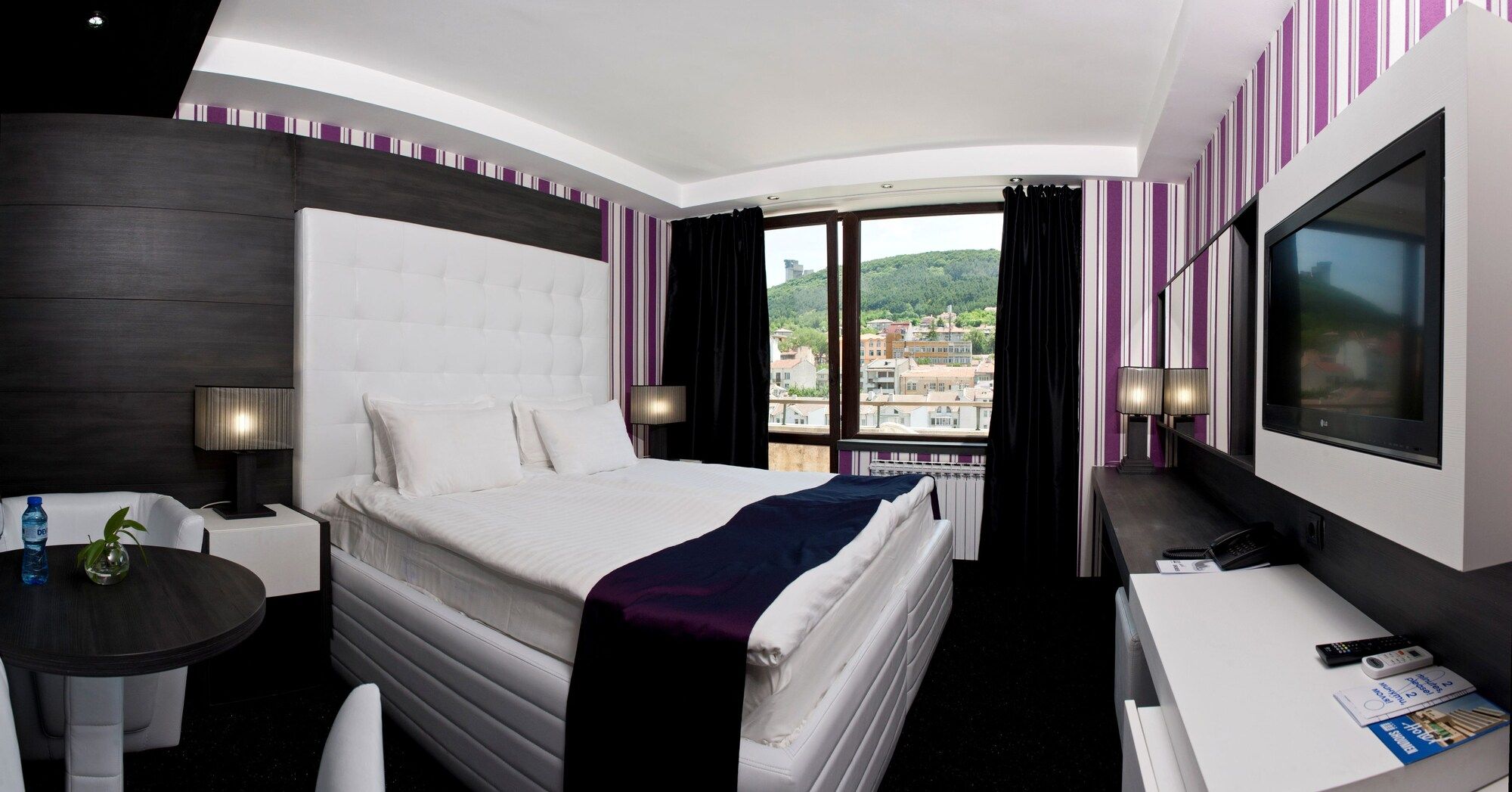 Una camera d'albergo con un letto, una scrivania, una sedia, una televisione e vista sulla città.