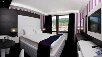 Una camera d'albergo con un letto, una scrivania, una sedia, una televisione e vista sulla città.