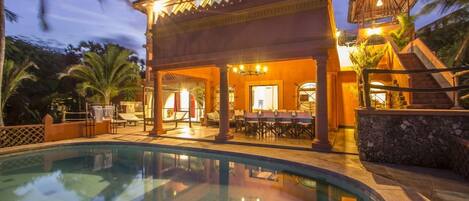 Uma área de piscina com um espaço de estar coberto, uma piscina e uma escadaria que leva a um segundo andar.