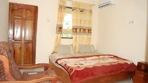 Ein Schlafzimmer mit Holztür, einem Bett mit blumigem Überwurf, einem Stuhl und einem Fenster mit Vorhängen.