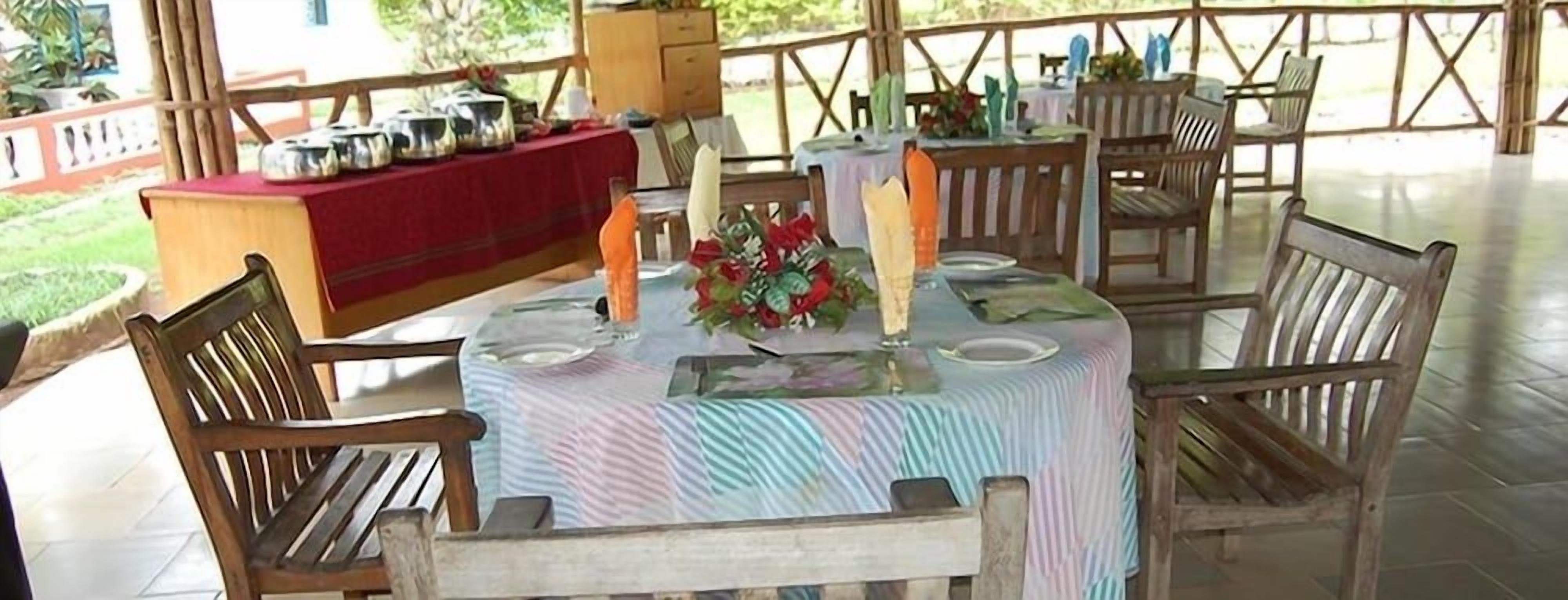 An outdoor dining area with wooden chairs and tables, a buffet setup, and a garden view.