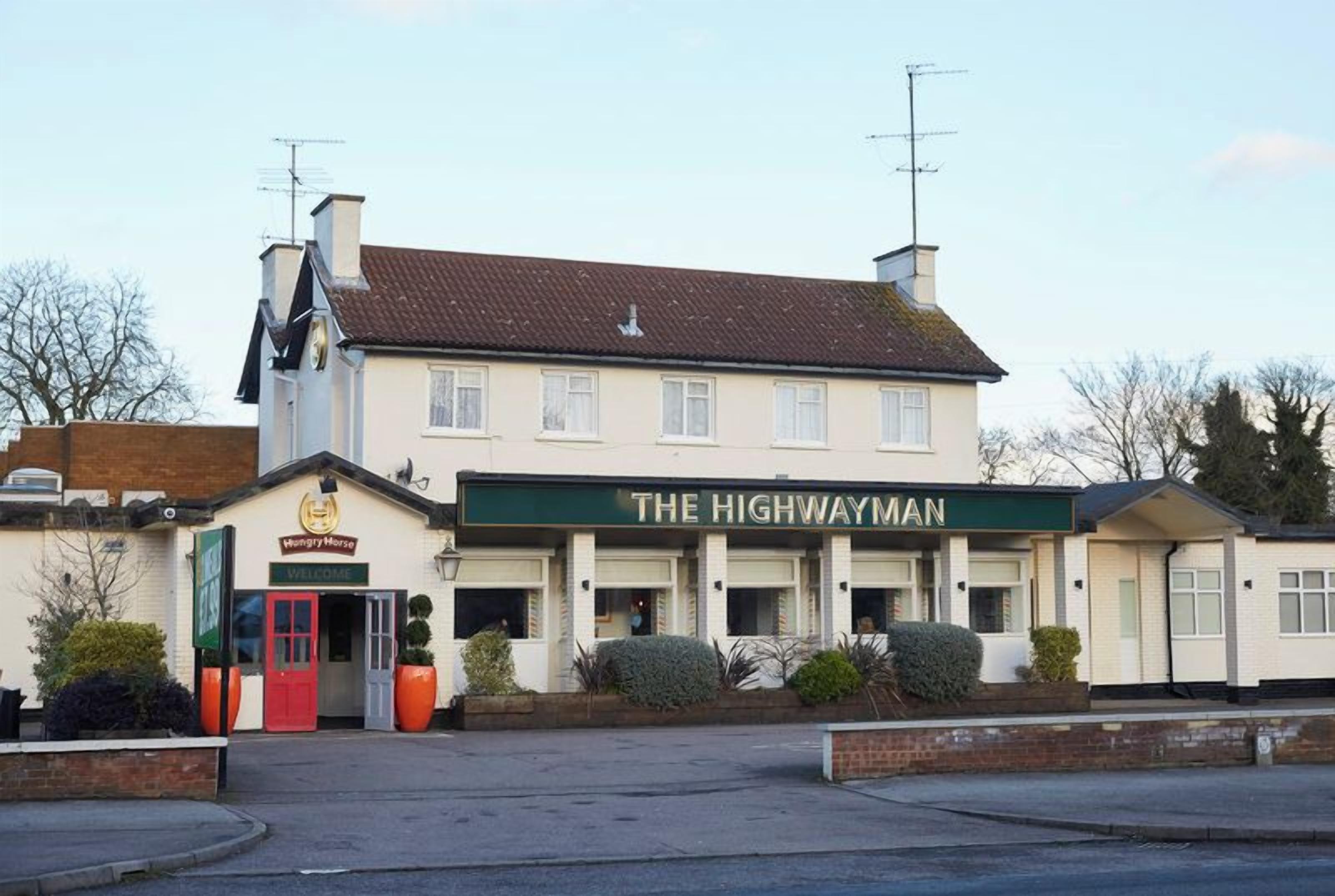 Un edificio de dos pisos con un letrero que dice 'THE HIGHWAYMAN' y una puerta roja.