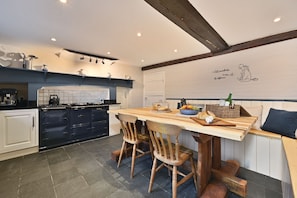 A kitchen with dark blue cabinets, a wooden table, and chairs. There is a white door and a wall with a drawing. - Blackham Farm  -  a holiday let sleeping 14 guests  in 6 bedrooms (Tunbridge Wells)